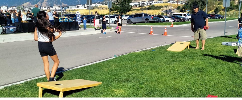 Families playing cornhole and a bbq in the background at a Kelsey Peak In-person Activity