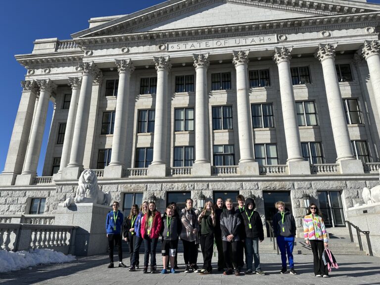 A group of students stand in front of the Utah State Capitol